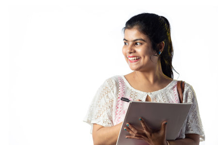 Portrait of a happy pretty young Indian girl taking notes and looking sideways on white backgroundの写真素材