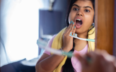 An Indian woman female girl in front of mirror facing dental problem while brushing teeth on white backgroundの写真素材
