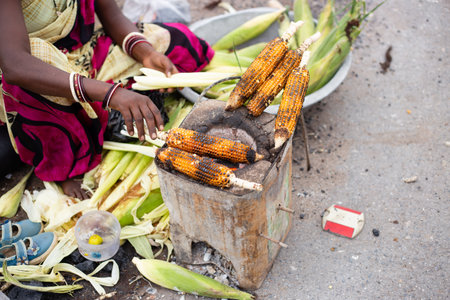 An unidentifiable Indian poor woman selling roasted corn at street or road side shopの写真素材