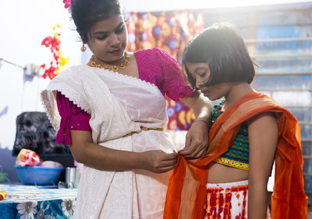 An Indian mother helping her girl child to wear traditional dress saree indoors at a festival nightの写真素材
