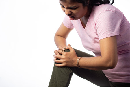 A person holding their knee in pain showing painful expression on white background