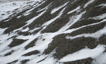 Dark grey sand dune with stones and snowの写真素材