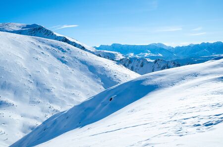 Snow hills of mountains in a sunlight, shadows and a blue skyの写真素材