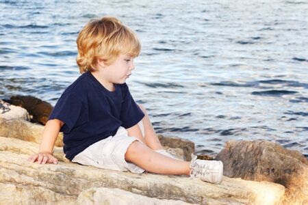 a young boy sitting on the edge of a lakeの写真素材