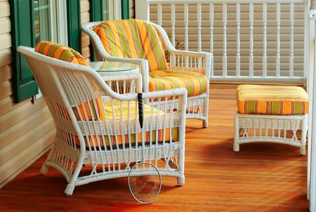 A badminton racket rests against a wicker chair on the porch of a houseの写真素材