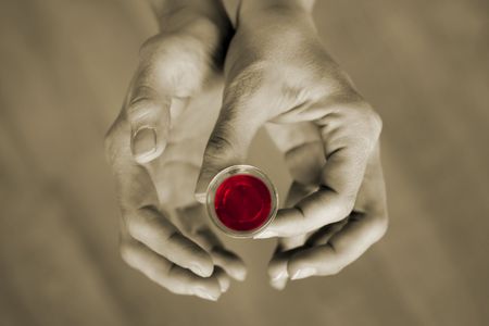 Hands holding a communion cup, the wine is red and the rest of the image is subdued colorの写真素材