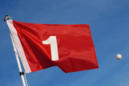 A red golf flag with the number 1 against a blue sky backgroundの写真素材