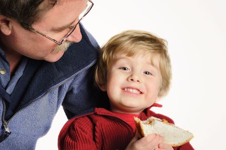 Father smiling at son who is holding a peanut butter and jelly sandwichの写真素材