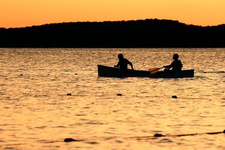 Two canoers row across a lake at sunsetの写真素材