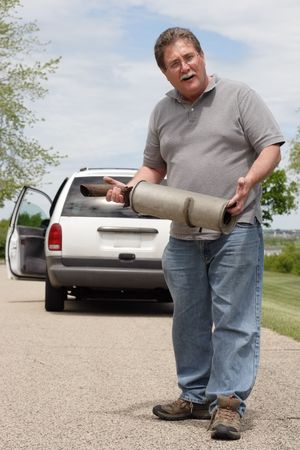 A man holds the muffler that just fell off of his carの写真素材