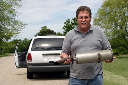 A man holds the muffler that just fell off of his carの写真素材