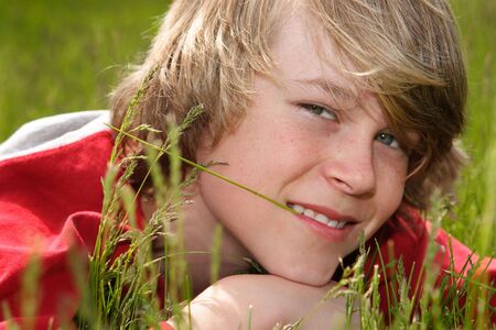A teenage boy laying down chewing on a blade of grassの写真素材
