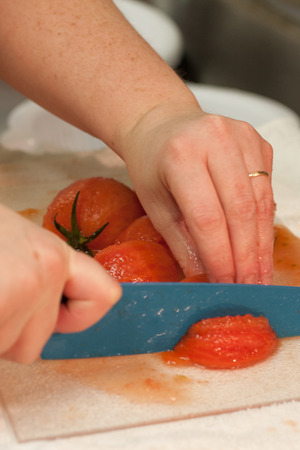 Fresh tomatoes being diced on a cutting board by a female chef with a ceramic knife.の写真素材