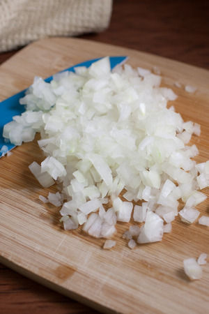 Fresh chopped onions and a blue ceramic knife on a wooden cutting board.の写真素材