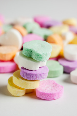 Pastel colored candy hearts in a pile on a white surface.の写真素材