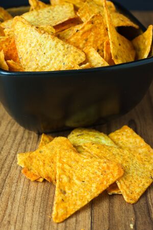 Nacho cheese flavored tortilla chips in a dark bowl on a wooden table.の写真素材