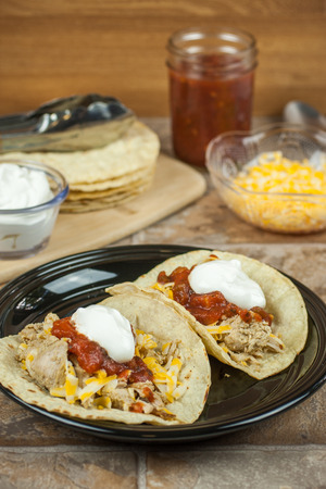 Pork carnitas with corn totillas on a dark plate with ingredients in the background.の写真素材