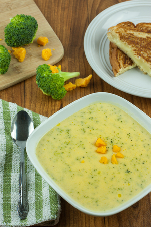 Broccoli cheese soup in a white bowl with a grilled cheese sandwich on a wooden table.の写真素材