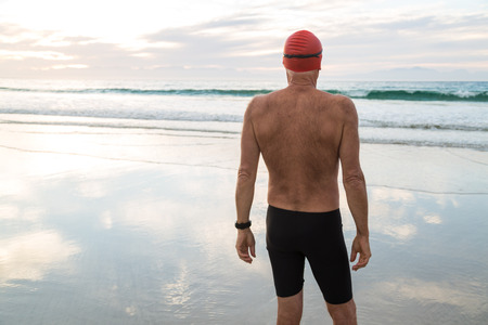 Senior man, aged 65, preparing to swim in the sea at dawnの写真素材