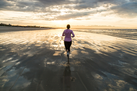 Young female runner jogging on a  beach at sunriseの写真素材