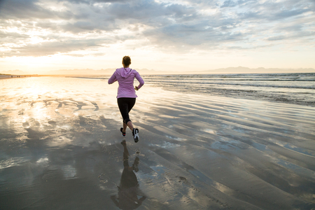 Young female runner jogging on a  beach at sunriseの写真素材