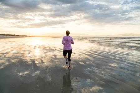 Young female runner jogging on a  beach at sunriseの写真素材
