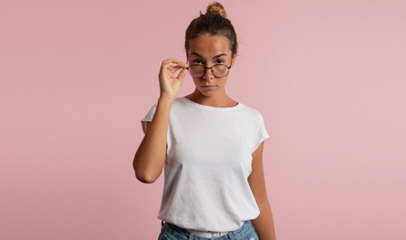 Young Woman holding eyeglasses and Looking Over them isolated over pink backgroundの写真素材