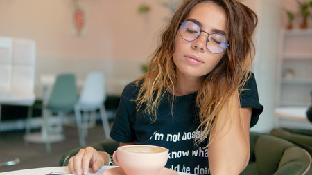 A portrait of cute young female, she closed her eyes with joy, she smelling her fresh coffee in the...