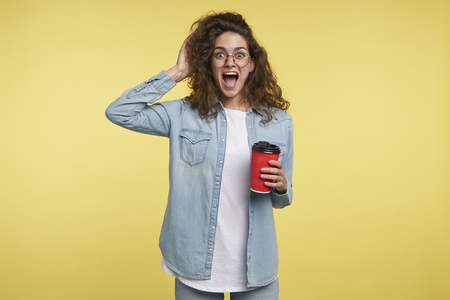 Happy screaming brunette italian woman having a coffee in the morning, she got inspired by new idea, isolated over yellow backgroundの写真素材