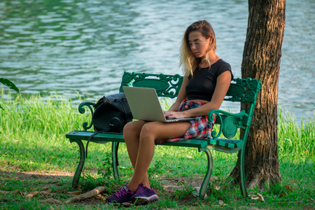 student girl in black T-shirt and shorts outdoors, sitting on bench by pondの写真素材