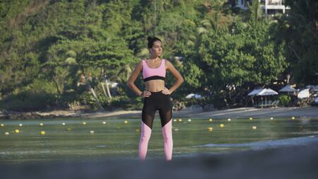 athletic yoga girl posing on sunny white sand beach, wearing pink top and shortsの写真素材