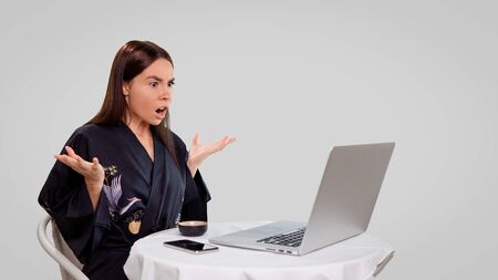 woman works freelance from home, she use her laptop computer to read fresh news, she got surprised, she wears home asian robe and isolated over whiteの写真素材