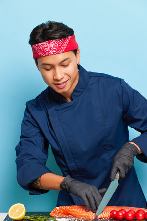 Close up photo of young Asian chef inside the studio preparing fillet of fresh fish with knife for...