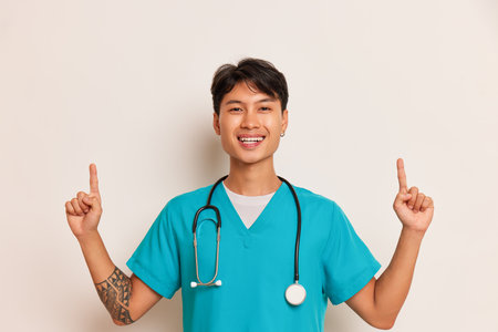Kind doctor stands on white background, folding fingers of his hands up, smiling at camera, professional people concept, copy spaceの写真素材