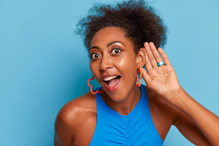 Close up photo of happy black girl in blue top against blue background, holding one hand near her...