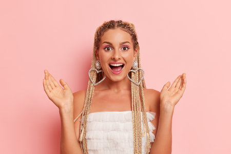 Portrait of happy girl in white top with long dreads posing on pink background, with open mouth and hands up, happy time concept, copy spaceの写真素材