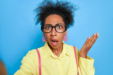 Close up shot of young black woman wearing glasses, really surprised and raises hand palm up during video call, excitement concept, copy spaceの写真素材