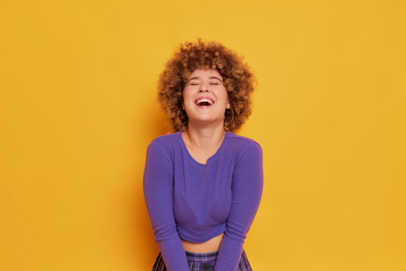 Young african american woman with curly hair laughing on yellow backgroundの写真素材