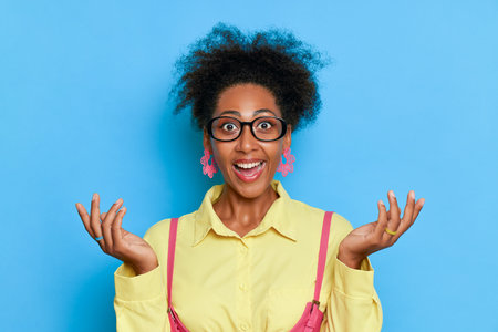 Portrait of excited african american woman in eyeglasses on blue backgroundの写真素材