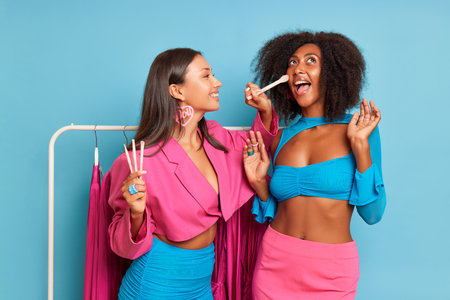 Two happy young african american women in bright clothes holding toothbrushes on blue backgroundの写真素材