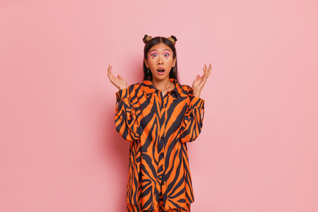 Oriental young woman dressed in zebra design shirt with two buns hairstyle, surprise on her face, hands up, copy space, wondering conceptの写真素材