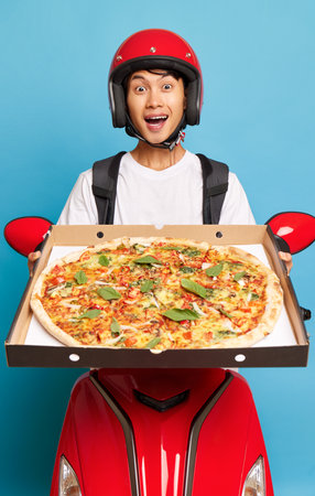 Delivery guy wearing red helmet sitting on his red scooter holding pizza box in hands, fast delivery concept, copy spaceの写真素材