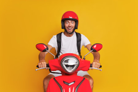 Delivery bearded guy on red scooter against yellow backdrop, wearing red helmet, holding handle bar with both hands, delivery service concept, copy space.の写真素材