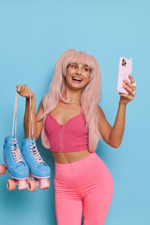 Attractive woman wearing style top and leggins posing on blue background with roller-skates and phone in hands and takes selfie, vintage fashion concept, copy spaceの写真素材