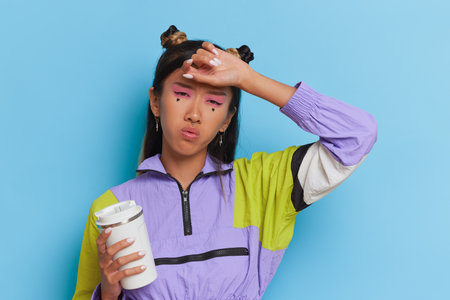 Japanese girl dressed in coloured sweatshirt stands on blue background, holding travel mug in hand, happy trip concept, copy spaceの写真素材