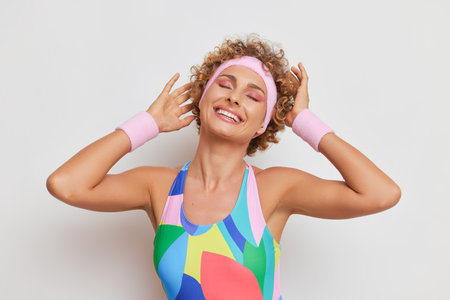 Portrait of smiling girl with short curly haircuts wearing colorful gymnastics skin-tight garment on white background with hands oevr her head, sports fashion concept, copy spaceの写真素材