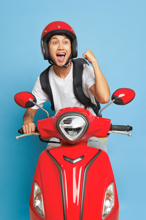 Happy oriental boy in red helmet rides on red motor bike, smiling and enjoying life, delivery service concept, copy spaceの写真素材