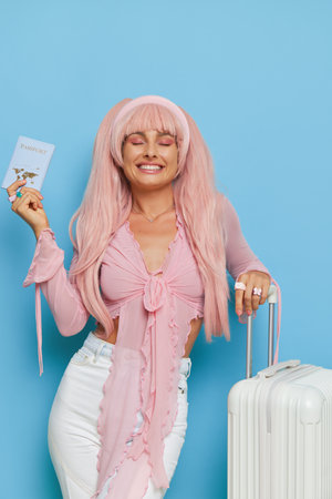 Close-up shot of pretty woman with pink long hair, wearing pink longsleeve top and white trousers standing on blue background, glamour style concept, copy spaceの写真素材