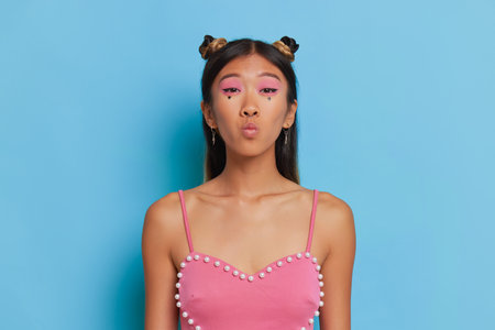 Korean woman with stylish makeup dressed in pink top posing isolated in studio, sending airkiss, amazing day concept, copy spaceの写真素材
