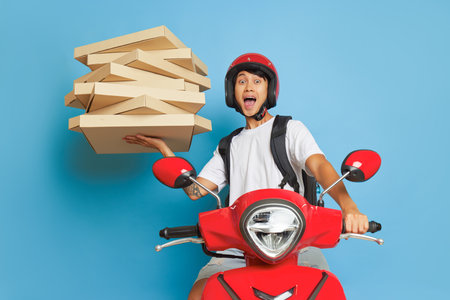 Courier guy riding red scooter on blue backdrop, holding pizza boxes in one hand, delivery concept, copy spaceの写真素材